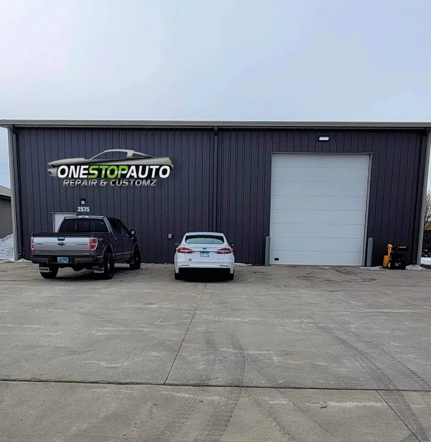 The dark steel shop building with the One Stop Auto sign and a white roll-up door