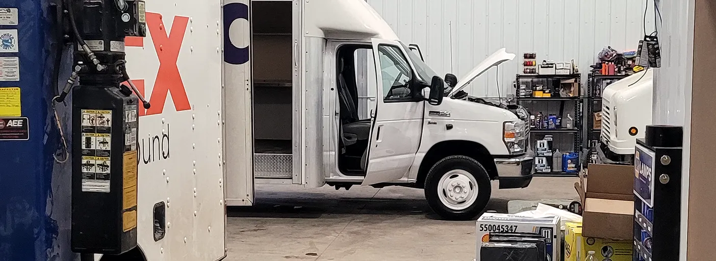 A white delivery van up on a blue lift in the shop, its hood open