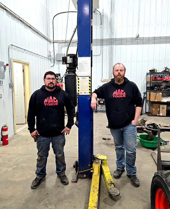 Mike Andre and Jake Brownell in the shop, either side of a blue lift post