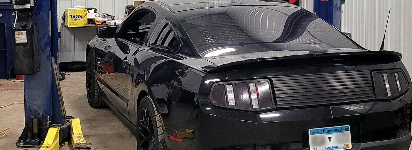 A black Mustang on the blue lift in the shop, seen from the rear