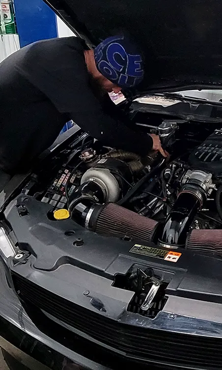 A mechanic leaning into an open engine bay with a turbocharger